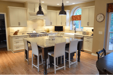 A remodeled white kitchen with light wood floors and square island in the middle with white stool seating on two sides. White tile backsplash.