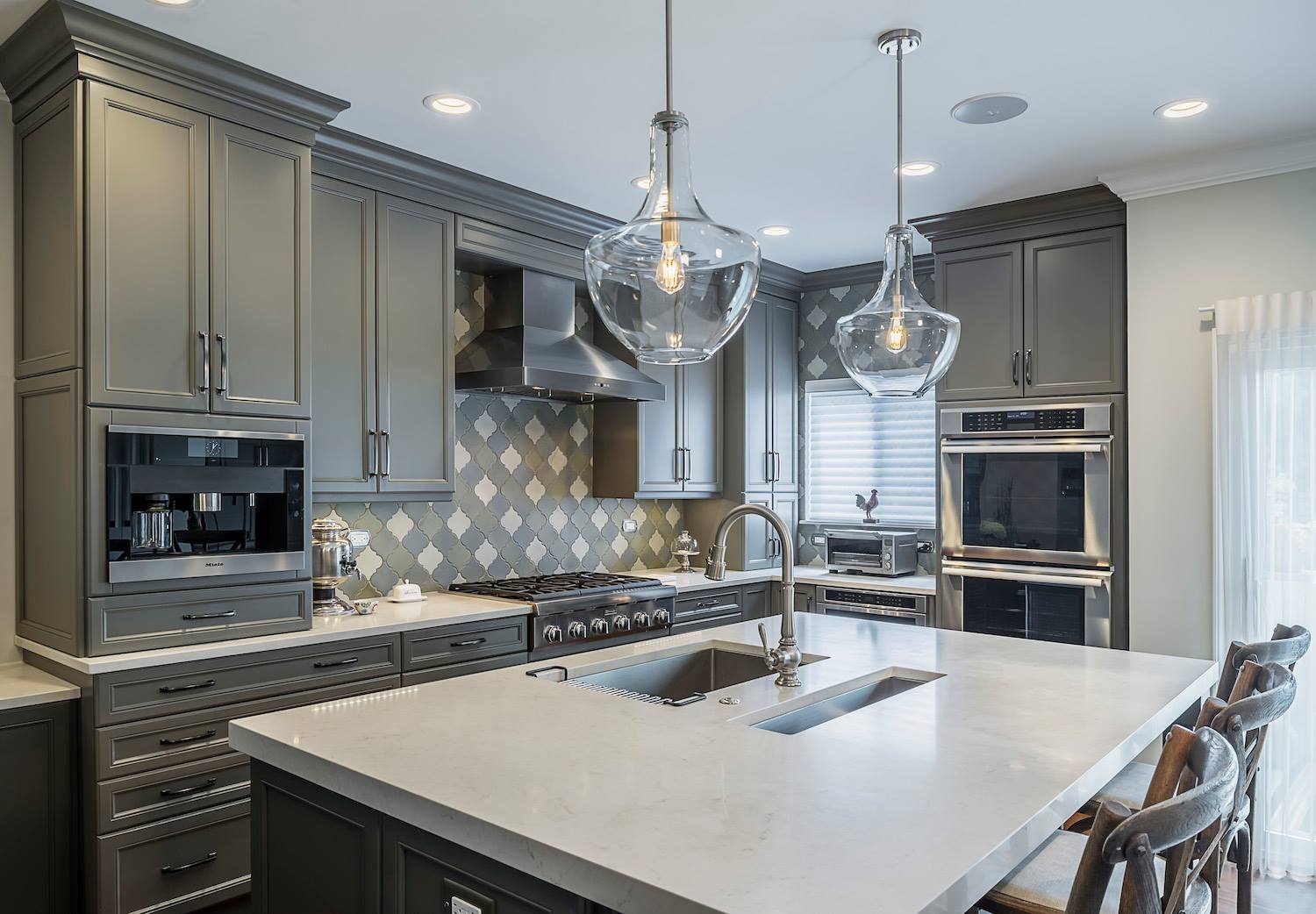 Custom gray kitchen with large center island, white stone countertops, glass pendant lights over island.
