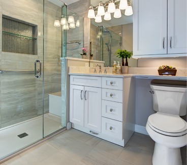 Remodeled bathroom with glass-enclosed shower, white vanity with stone countertop, and white tile floors.