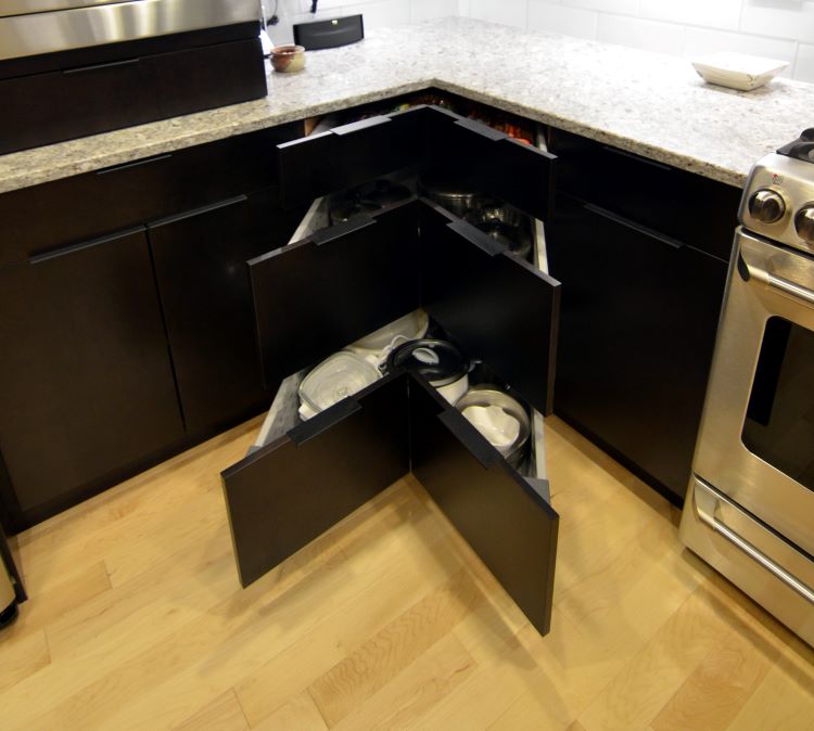 Black lower kitchen cabinets with three corner drawers partially pulled out. Light wood floors. White stone countertop.
