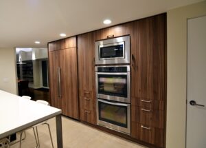 Remodeled kitchen cabinetry, modern woodgrain with wood-look fridge doors and stainless steel double ovens in the wall.