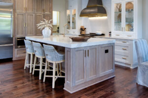 Remodeled kitchen with wood floors, white cabinets, white stone countertops, large island with stool seating and white-washed woodgrain cabinets.
