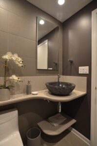 Remodeled bathroom with gray vessel sink and light gray/tan countertop and open shelf underneath.