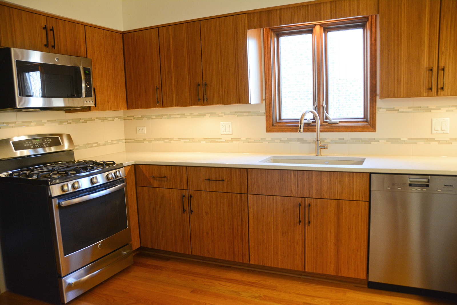 This modern kitchen has quartz counters and a glass tile backsplash
