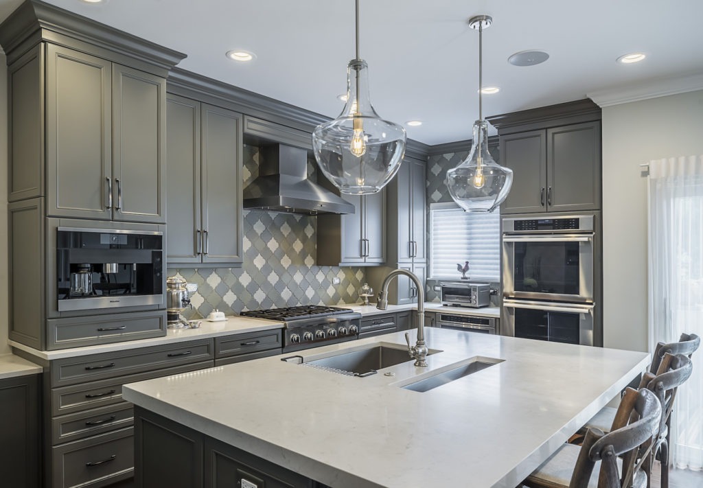Luxury kitchen with grey cabinetry and glass pendant lights over a large white stone island