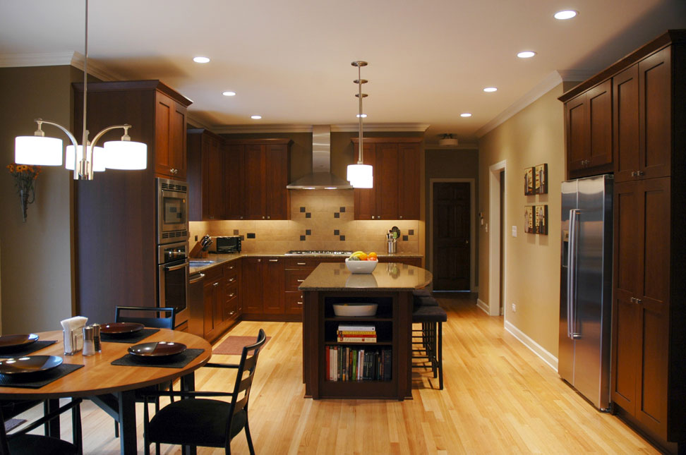 Kitchen remodel with light wood floors, dark wood cabinets, island with stool seating on one side, and small round dining table in foreground, to the left.