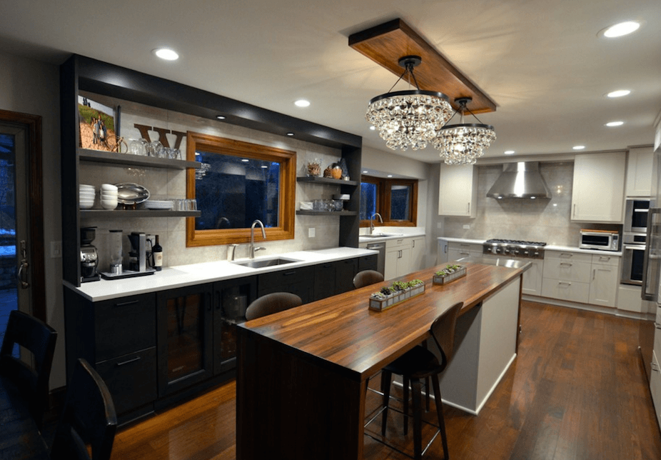 Remodeled kitchen with wood floors, black and white cabinets, long island with stool seating and butcher block countertop, chandelier-style pendant lights over island.