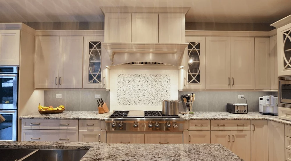 Kitchen with white cabinets, hooded vent, tile backsplash, and glass cabinets