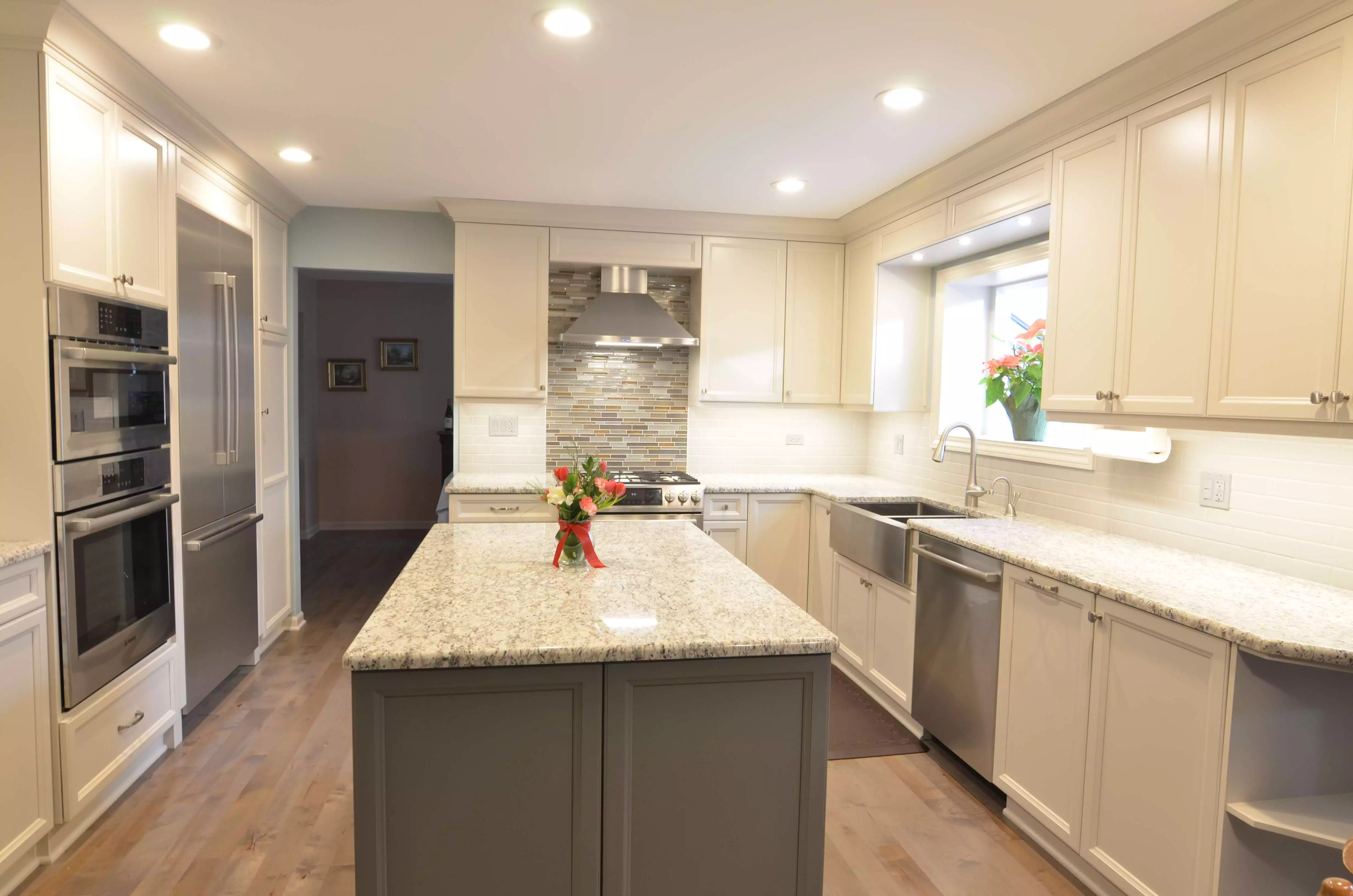 large bright kitchen remodel recess lighting white cabinetry hooded vent tile backsplash