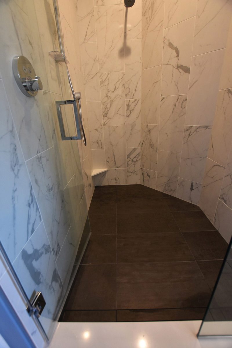 Walled-in shower with glass doors, marble walls and tiled floor
