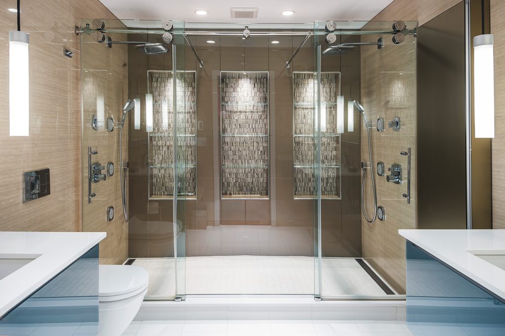 Bathroom with large shower glass doors chrome finishes two showerheads stone backsplash