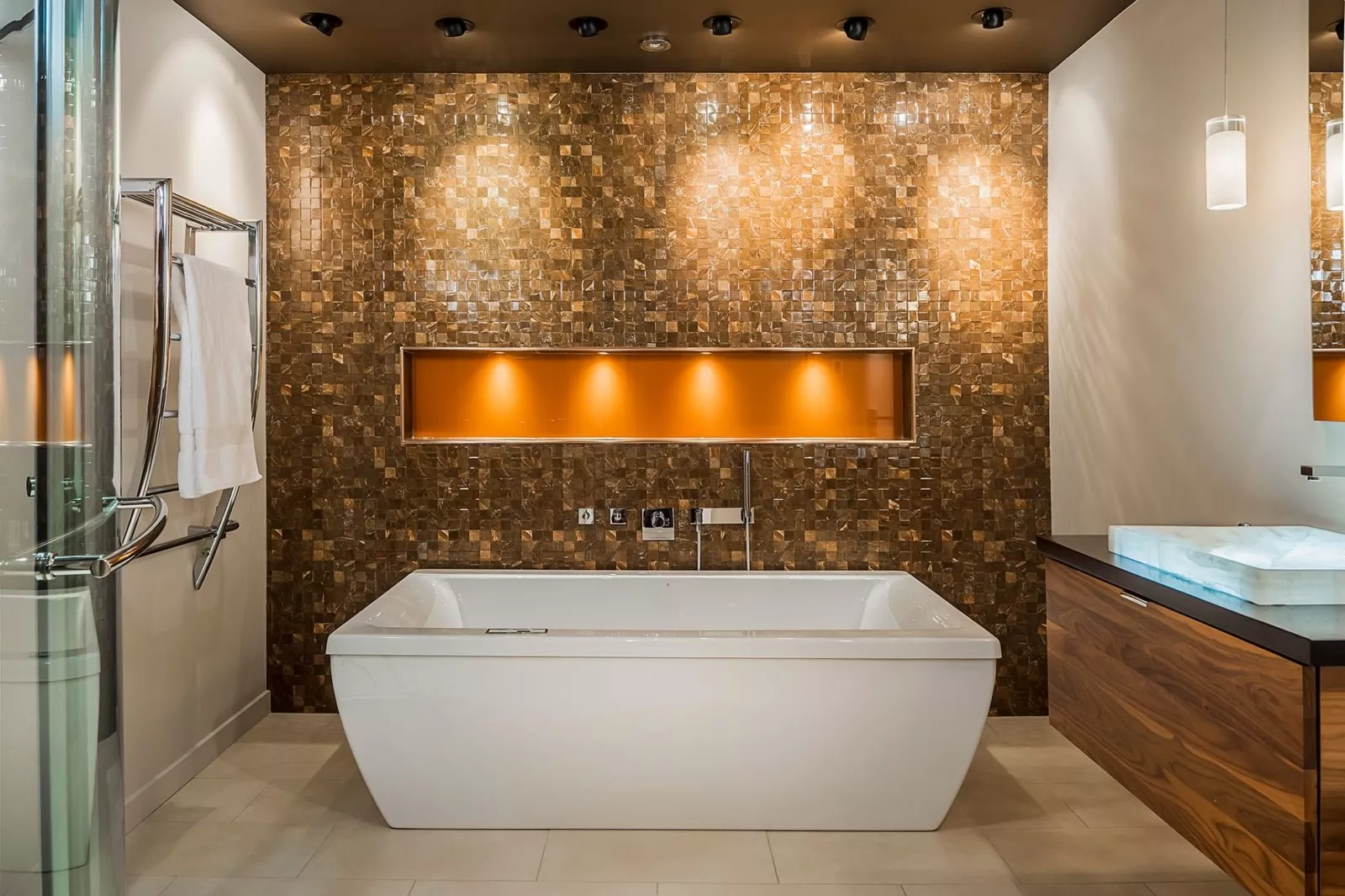 Free-standing white bathtub in a bathroom with brown tiling on one wall