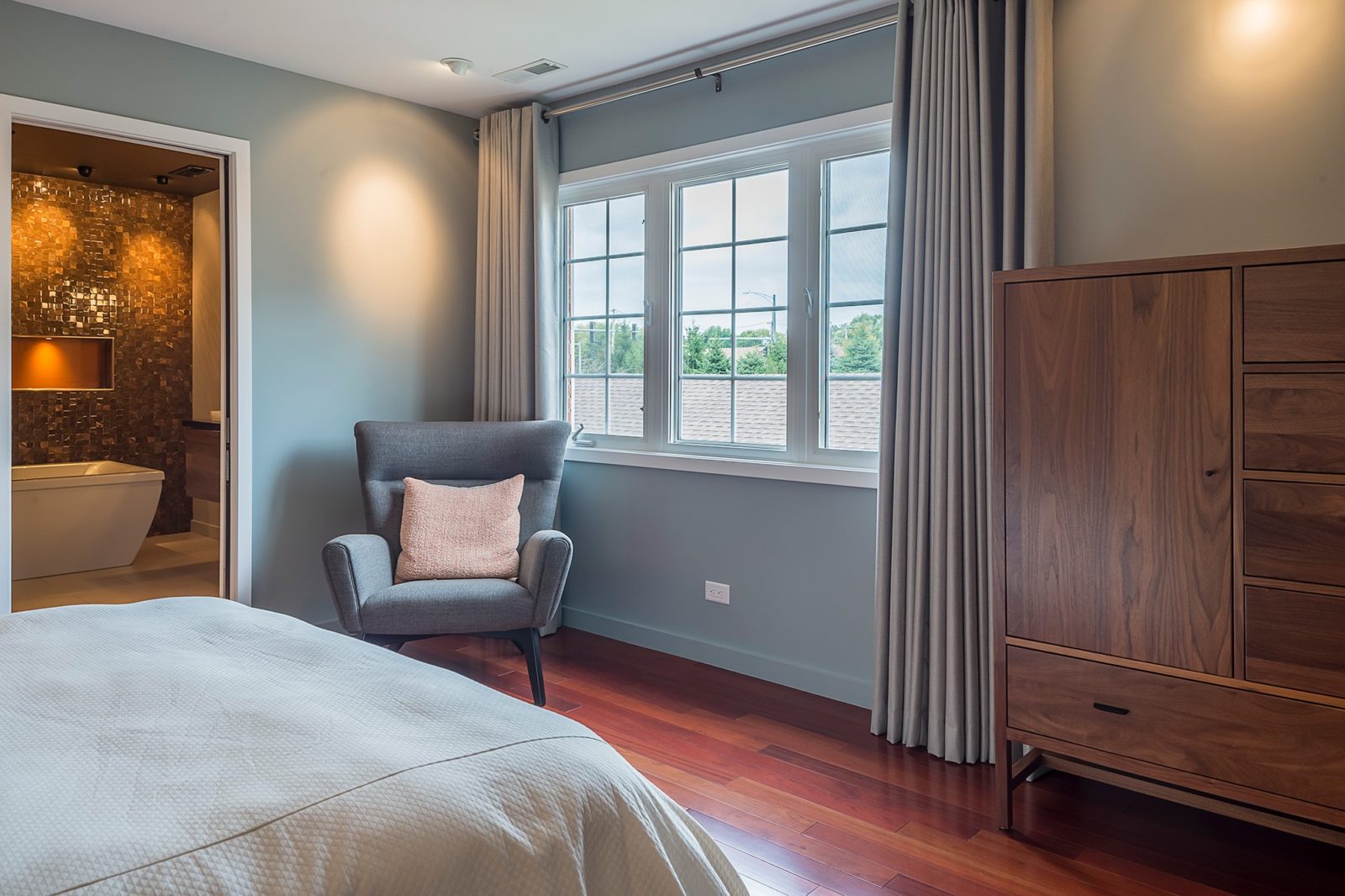 Bedroom with bed, chair, dresser, windows, and open door to adjacent bathroom