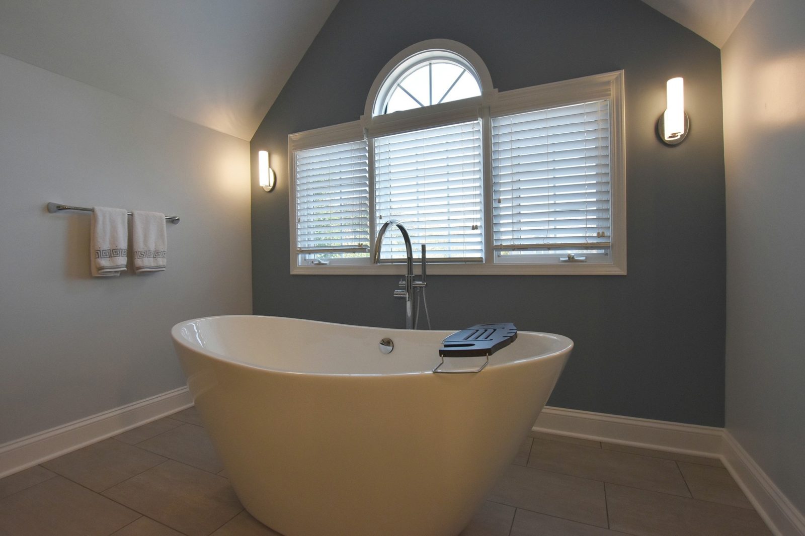 Free-standing white bathtub in a bathroom with windows behind it