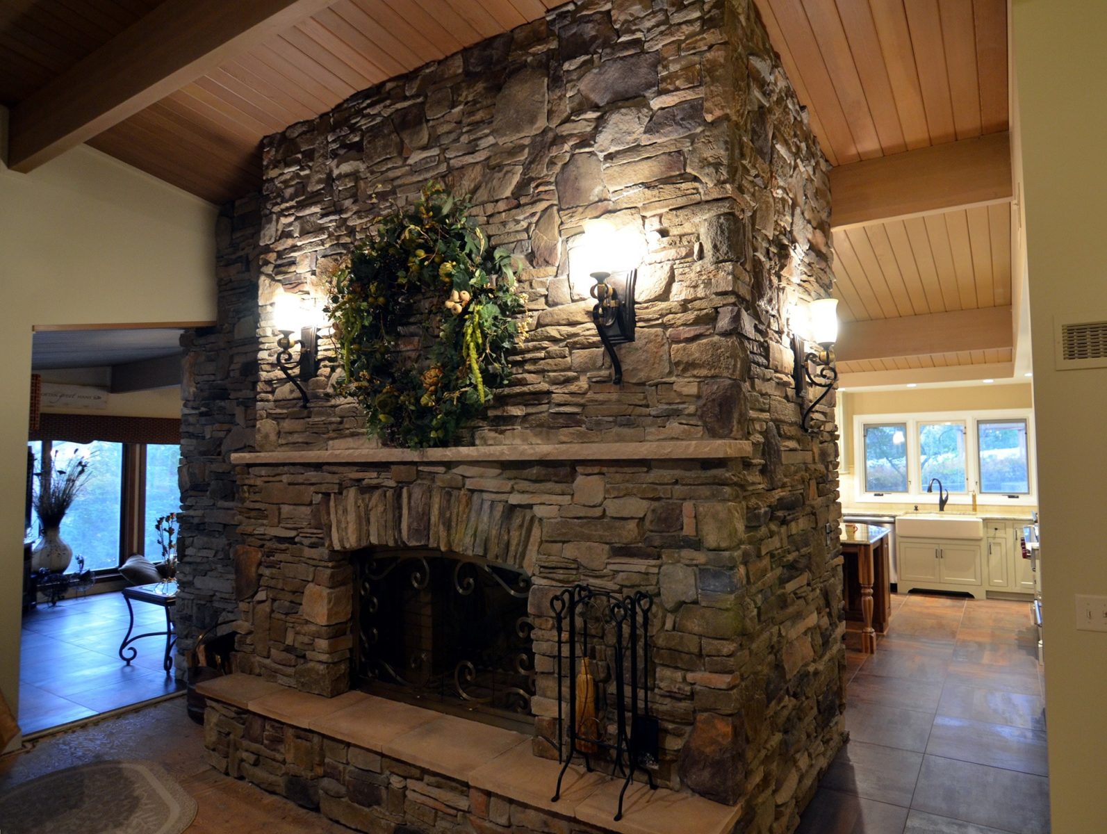 Large stonework fireplace with mantle and hallways leading to kitchen and living room