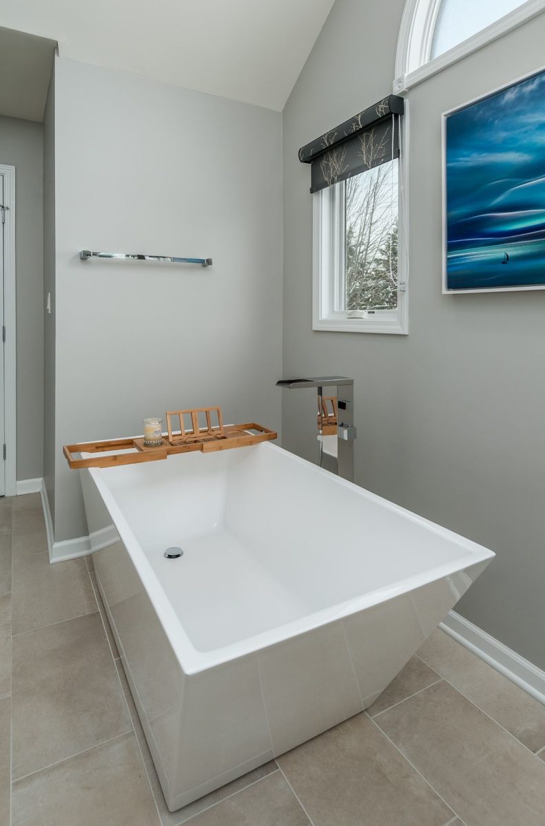 White free-standing bath tub with wooden tray in a bathroom with a small window