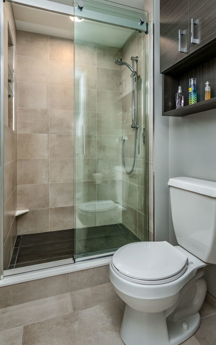 Bathroom with toilet and shower with glass doors and tiled walls and floor