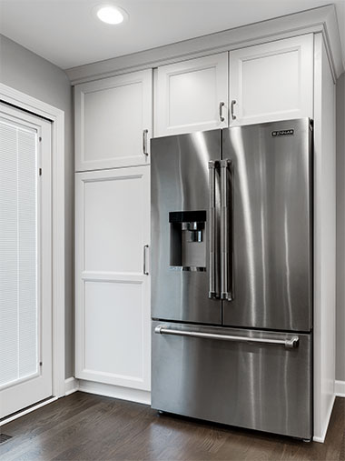 Kitchen wall with silver refrigerator and white cabinets framing it above and on one side
