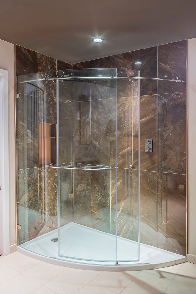 Corner shower with curved glass door and brown tiled walls