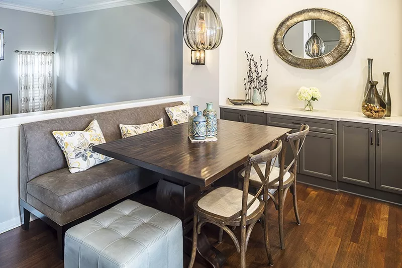 Home dining area with hardwood floors long couch seating ottoman wooden table bar with grey cabinets