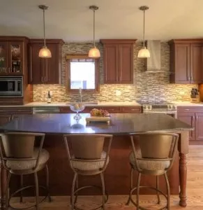 Kitchen with oak cabinets tiled backsplash ceiling to countertop black stone island pendant lights
