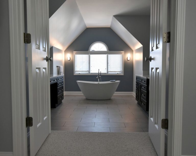 Bathroom with white garden tub centered on window two vanities tiled flooring french doors