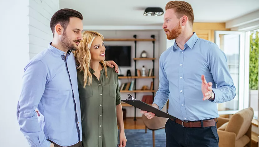 smiling couple being shown renovation plans by smiling man in middle of home