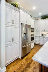 Remodeled kitchen with stainless steel fridge set into white cabinets. Wood floors. Recessed lighting.