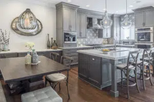 Remodeled kitchen and dining area with wood floors, gray cabinets, stone countertops, large island with seating, and dining table to the left.