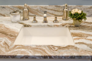 Tan and white marble bathroom countertop with white square sink and brushed nickel faucet.
