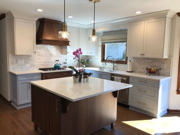 Remodeled kitchen with wood floors, white cabinets along walls, woodgrain island, all white stone countertops, white textured brick backsplash.